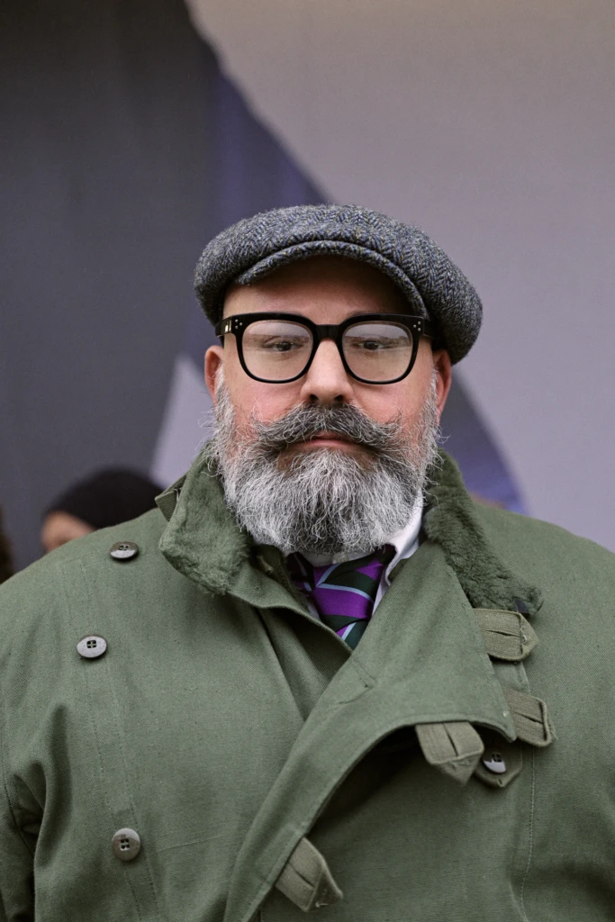 Man in a grey newsboy cap and green field jacket with a purple striped tie, Pitti Immagine Uomo 109 fair, Florence