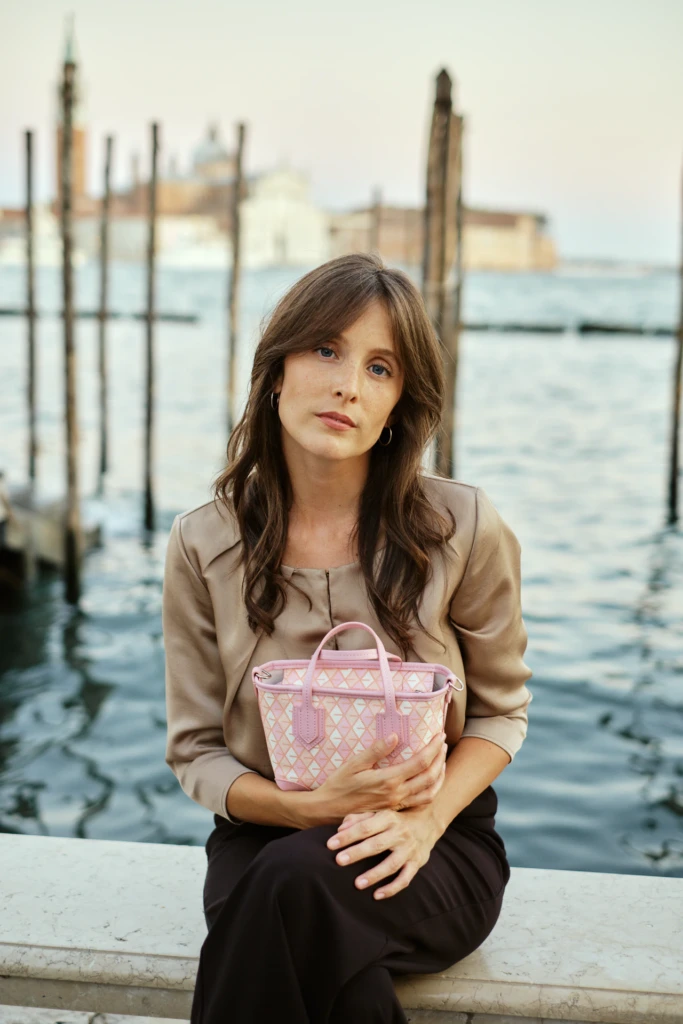 Woman seated by a Venice canal with a Vonto pink monogram mini leather handbag resting on her lap