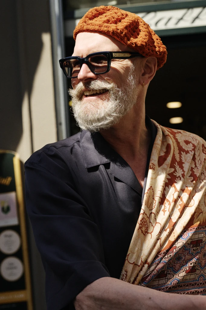 Man wearing an orange crochet beanie and black sunglasses with a patterned neckerchief at Pitti Uomo