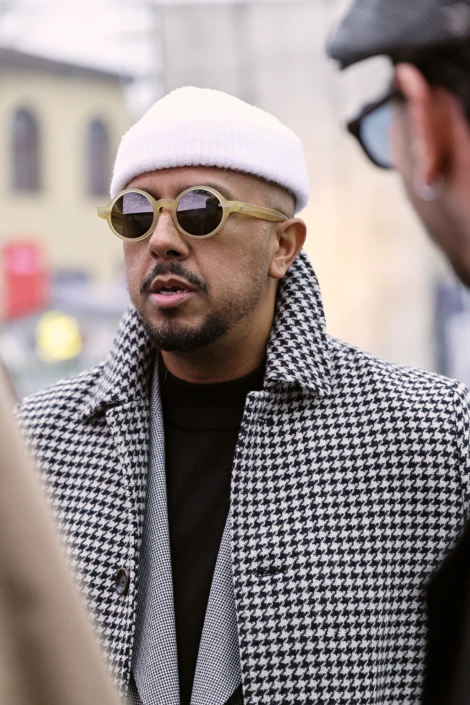 Man in a white knit beanie and round cream-frame sunglasses wearing a black houndstooth coat, Pitti Immagine Uomo 109 fair, Florence