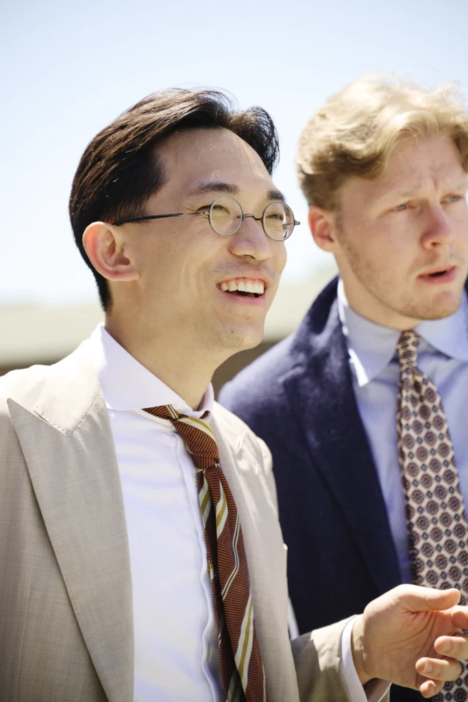 Two men in tailored jackets, one in beige with a striped tie laughing, the other in navy with a patterned tie