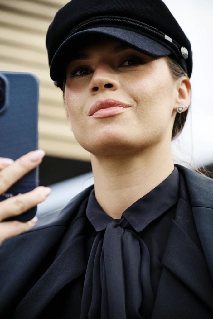 Woman taking a selfie in a black newsboy cap and black blouse with a bow collar, Pitti Immagine Uomo 109 fair, Florence