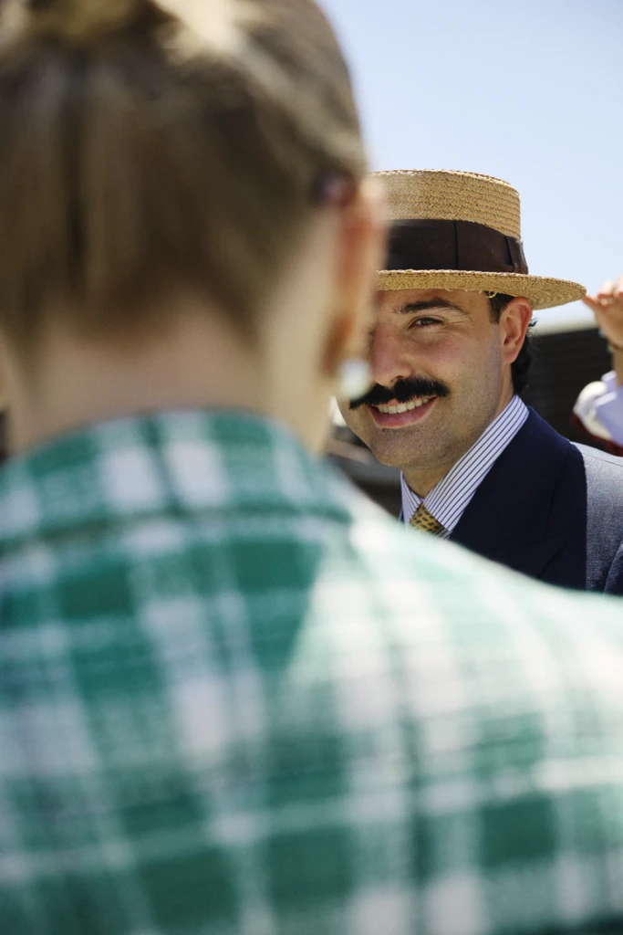 Smiling man with a mustache wearing a straw boater hat with a brown band and a navy pinstripe suit