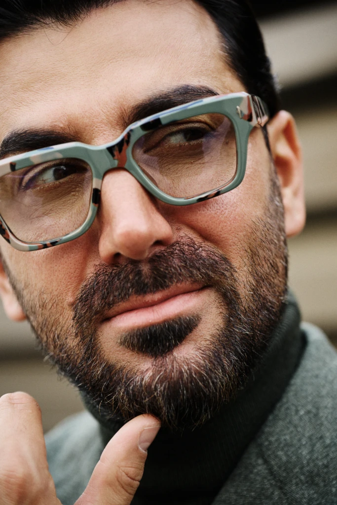 Close-up portrait of a bearded man in camouflage-pattern glasses and a grey turtleneck, Pitti Immagine Uomo 109 fair, Florence