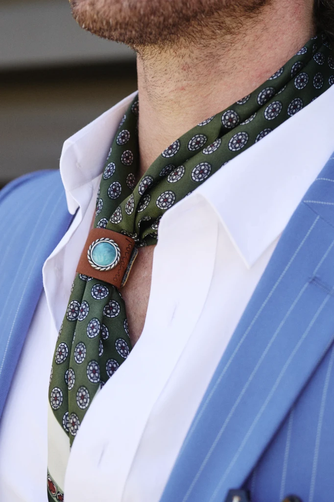 Close-up of an olive green medallion-print tie held with a leather and turquoise slide