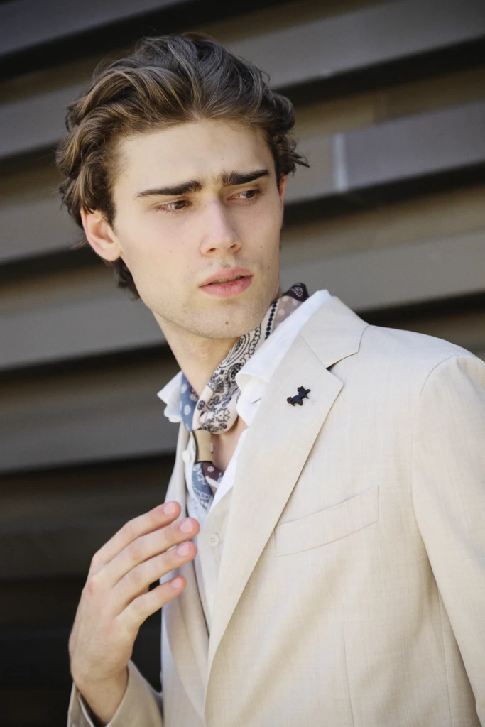 Man in a beige suit with a paisley neckerchief, looking off to the side