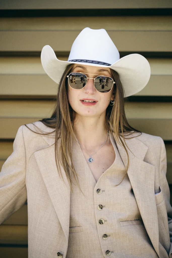 Woman in a white cowboy hat and aviator sunglasses wearing a beige waistcoat and blazer