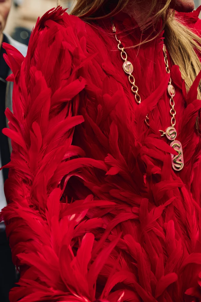 Close-up of a red feathered coat with a gold chain necklace featuring interlocking S charms, Milano Fashion Week street style detail