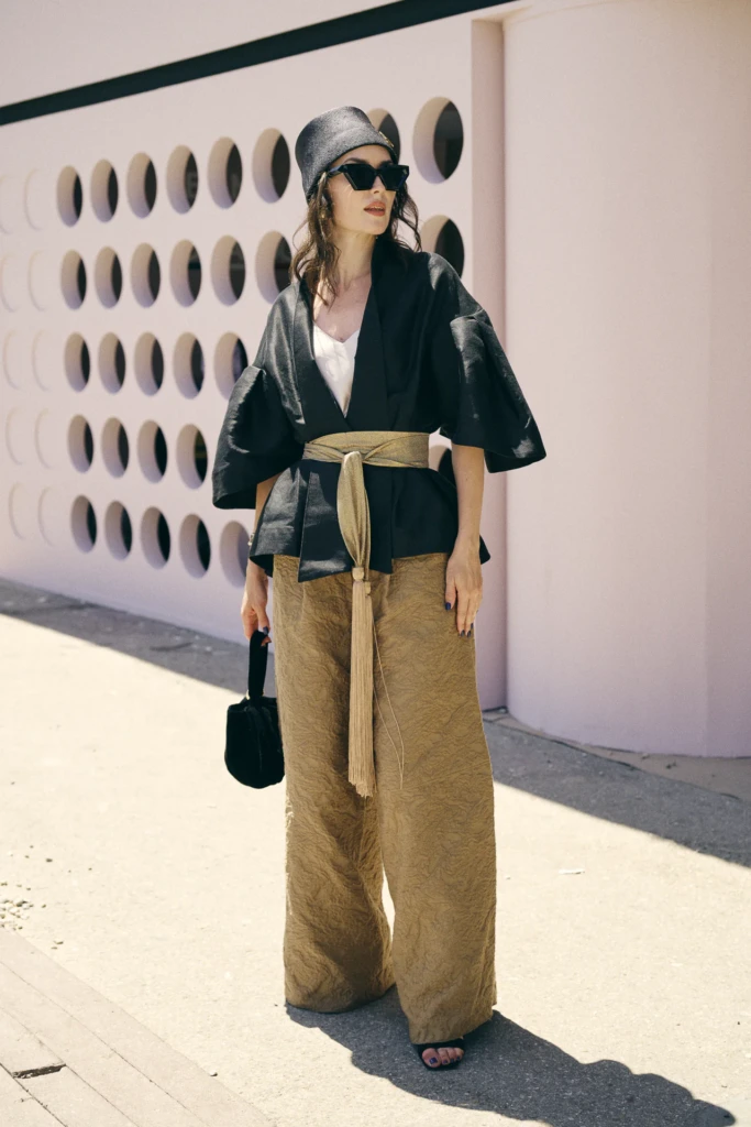 Woman in a black kimono-style jacket with a gold obi sash and beige textured trousers