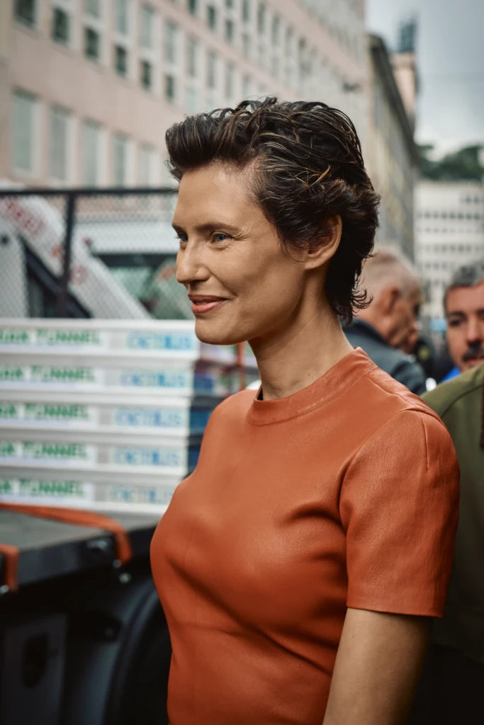 Bianca Balti with short dark wavy hair in a rust-orange leather top, seen in profile against a delivery truck stacked with Chanel-branded boxes, Milano Fashion Week street style