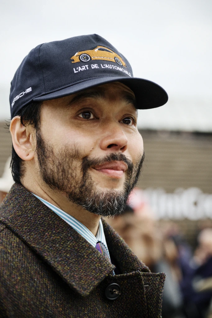 Man in a Porsche 'L'Art de l'Automobile' cap with long sideburns and a goatee, wearing a tweed coat, Pitti Immagine Uomo 109 fair, Florence