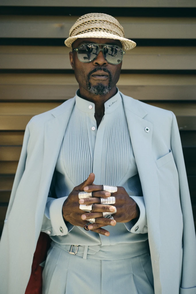 Man in a pale blue suit and straw boater hat with multiple silver statement rings