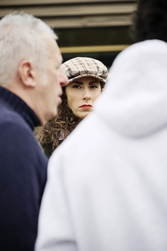 Woman in a plaid flat cap with curly hair looking over a man's shoulder in a crowd, Pitti Immagine Uomo 109 fair, Florence