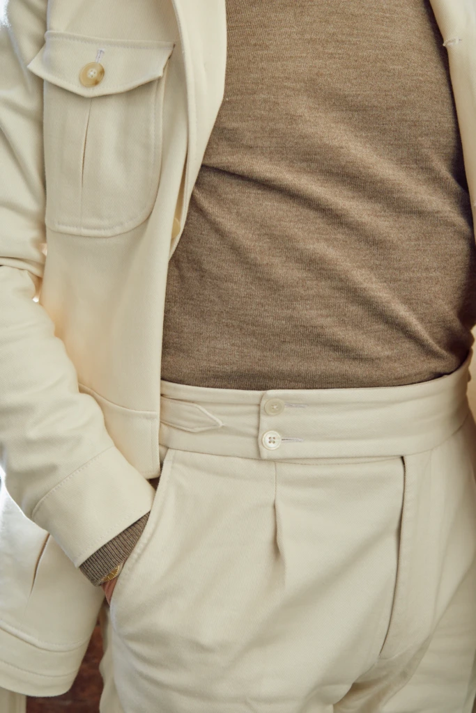 Fidelio Tailor editorial at Pitti Immagine Uomo 107, Florence — tailoring detail with cream overshirt, camel merino sweater and double-button pleated trousers.