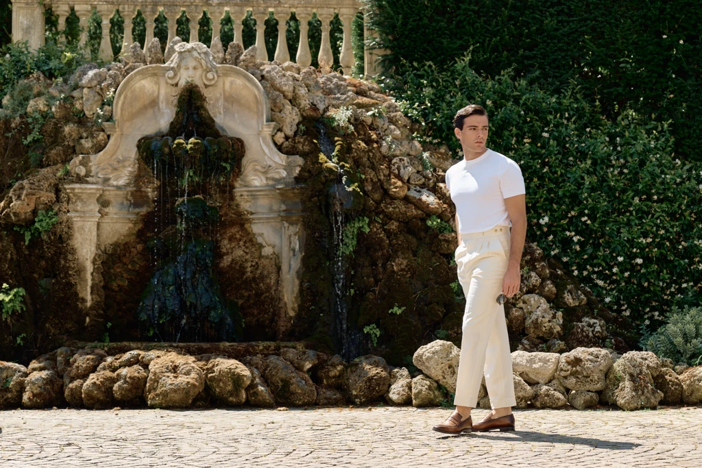 Common Suites Italian tailoring at Villa Cora Florence: model in high-waisted pleated trousers and knit polo climbing the villa's neoclassical stone steps.