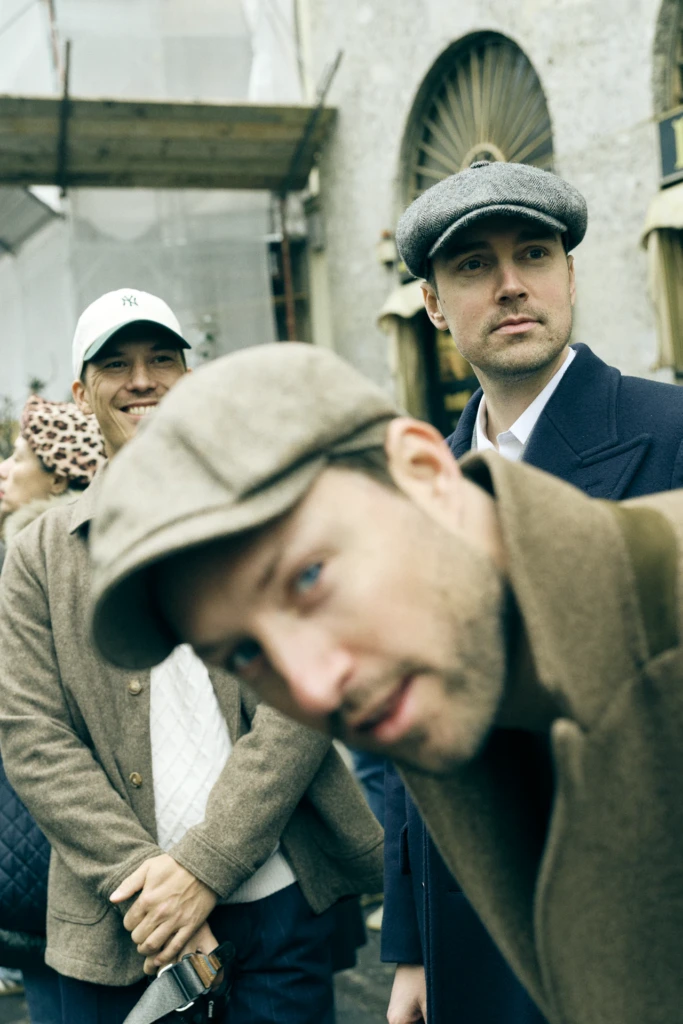 Group of men in flat caps and tweed jackets outside a Milan building with an ornate arched doorway, Milano Fashion Week street style, Milano Fashion Week, January '26