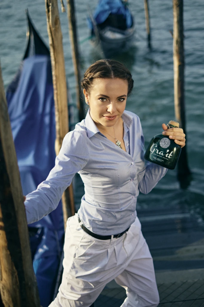 Model with braided hair presenting the Gra'it grappa bottle on a Venice gondola dock
