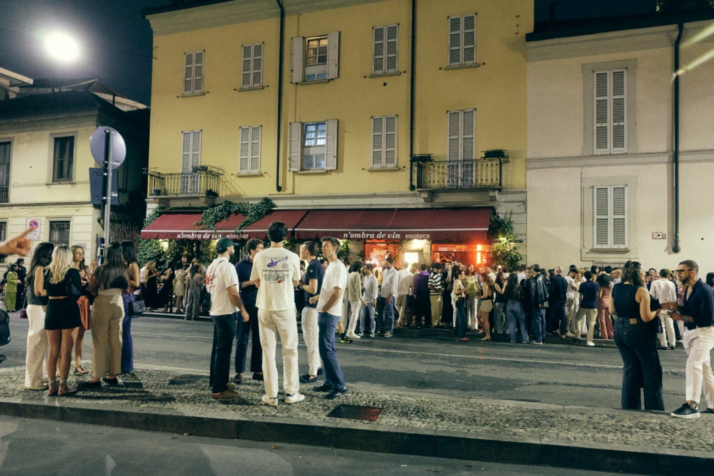 Crowded street scene at night outside n'ombra de vin wine bar in Milan, people gathered on the sidewalk during Fashion Week