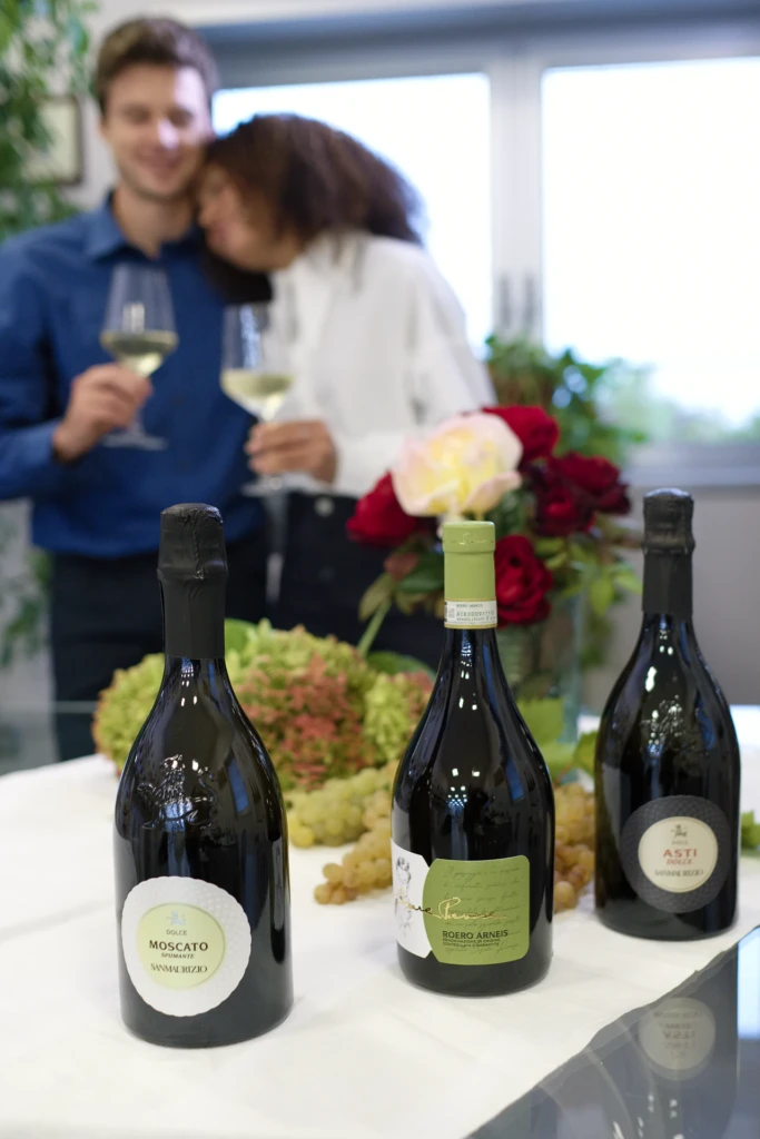 Two models sharing an embrace at the table beside a bottle of Barbera d'Asti