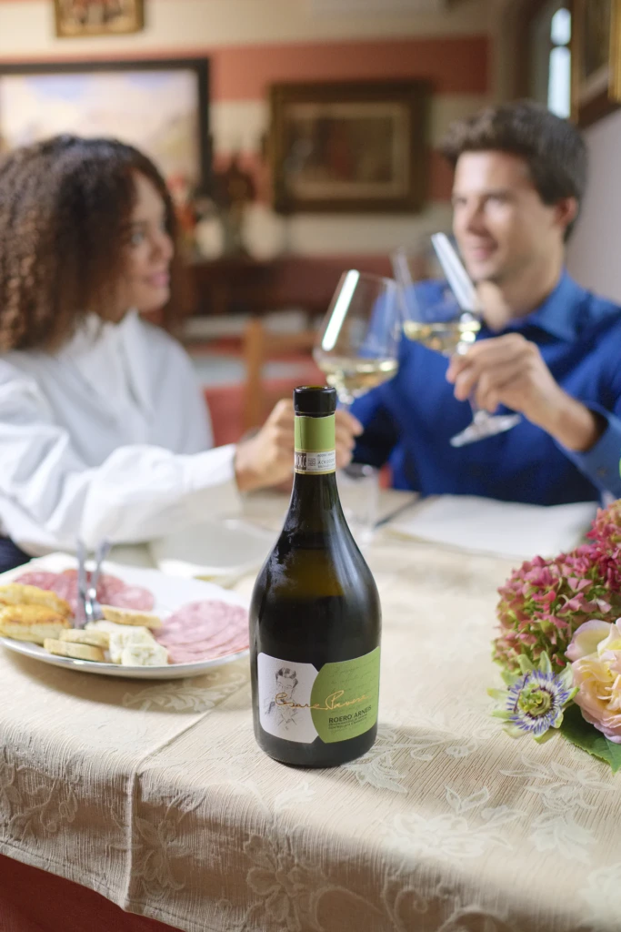 Two models toasting with white wine over a spread of charcuterie and cheese, a bottle of Roero Arneis on the table