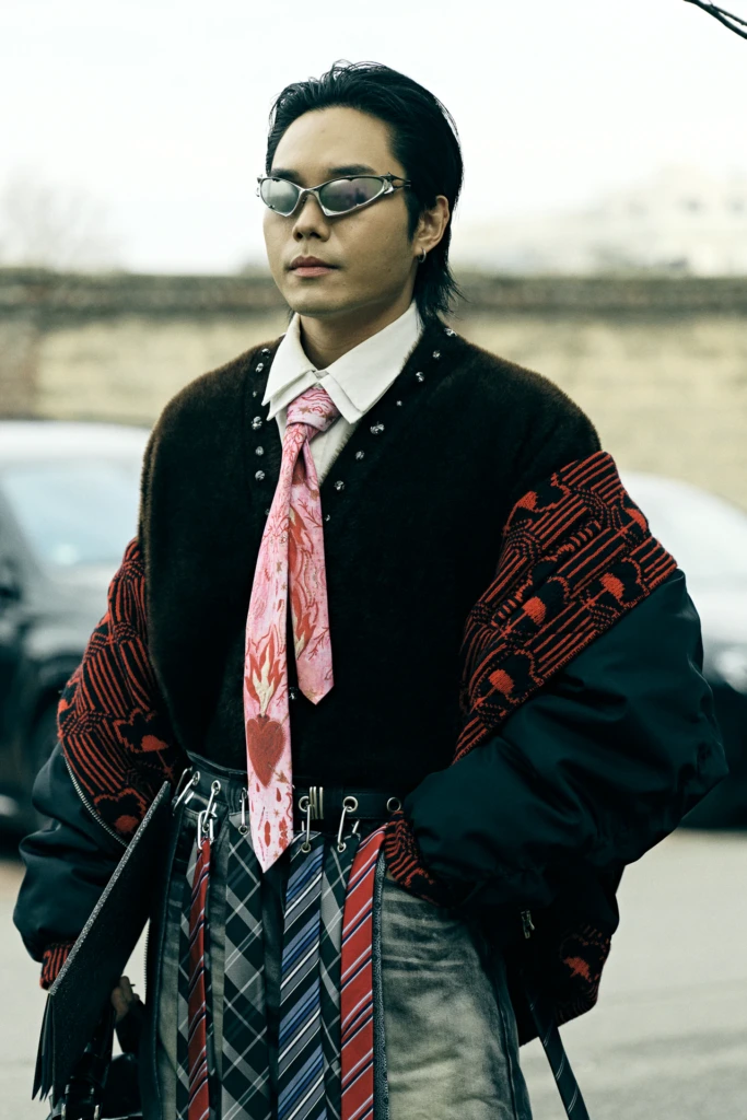Man in an embellished dark jacket wearing a pink heart-print tie over layered neckties clipped to his belt, Milano Fashion Week, January '26
