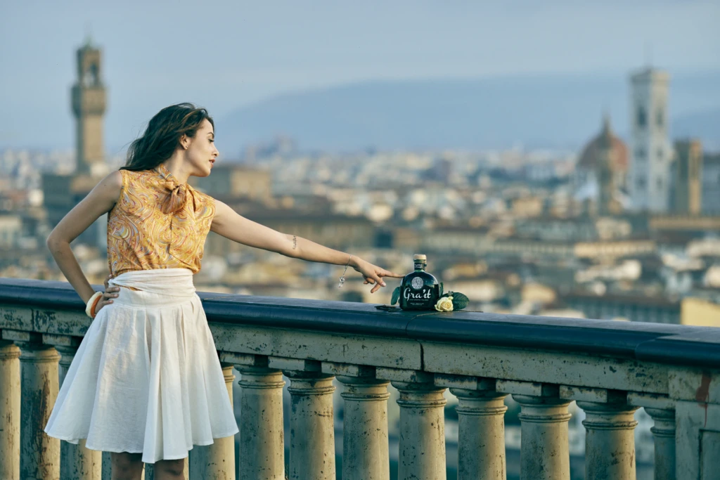 Model reaching toward the Gra'it bottle and a white rose on a Florence rooftop balustrade overlooking the Duomo