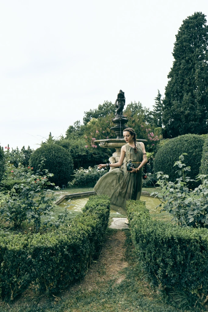 Model in a flowing dress holding the Gra'it bottle beside a stone fountain in a Florentine garden