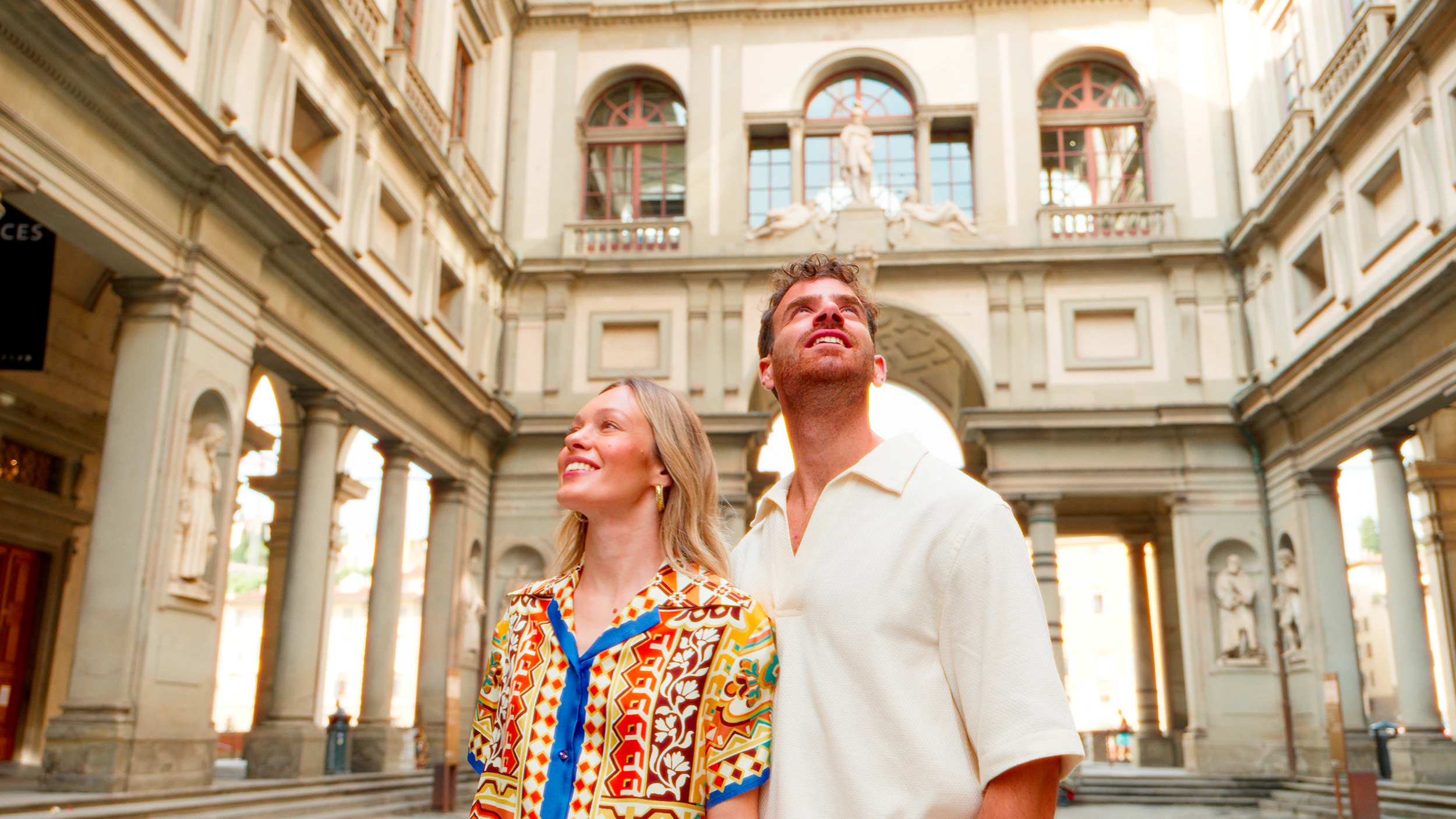 A couple gazing up at the Uffizi Gallery's arched loggia in golden Florence light