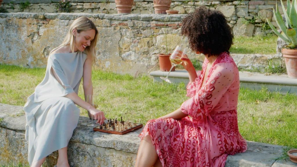 Two women playing chess with wine on a stone wall in a Florence garden